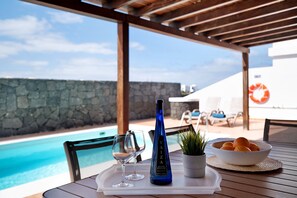 A poolside table with a bottle, glasses, and a bowl of fruit. - Vacation Home "Villa Rubí" with Sea View, Private Heated Pool und Wi-Fi (Playa Blanca)