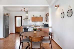 A modern kitchen with a round dining table, wooden cabinets, and a stainless steel refrigerator.