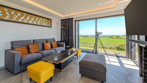 Ein modernes Wohnzimmer mit einer Couch, einem Hocker, einem Couchtisch und einem großen Fenster mit Blick auf die Landschaft.
