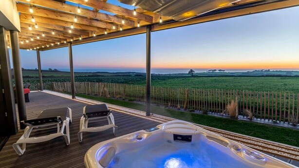 Ein Whirlpool mit Blick auf einen Sonnenuntergang über einem Feld, eine Holzterrasse und zwei Liegestühle.
