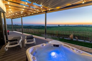 Ein Whirlpool mit Blick auf einen Sonnenuntergang über einem Feld, eine Holzterrasse und zwei Liegestühle.