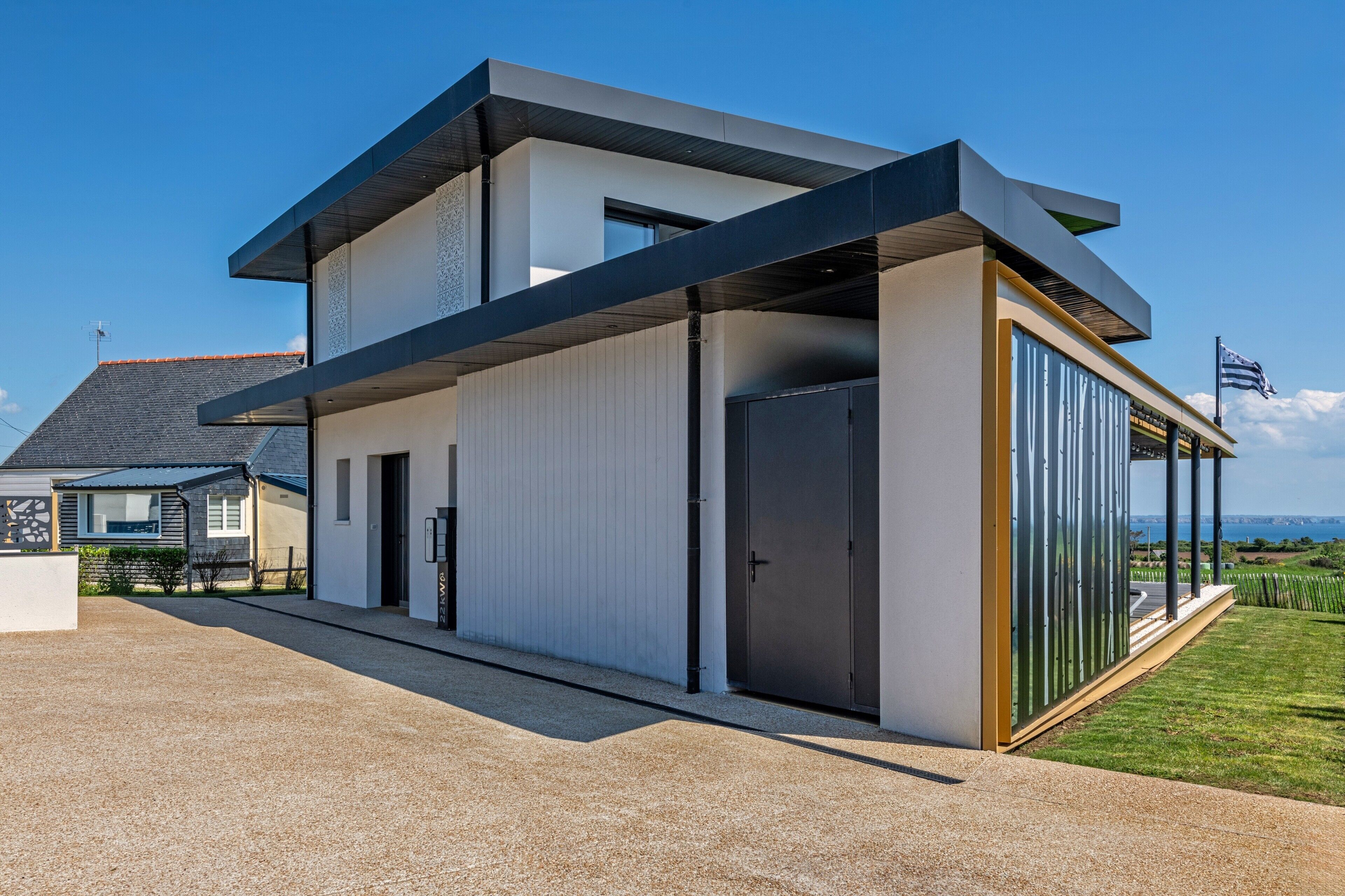 A modern two-story house with a large glass door, a covered outdoor area, and a view of the landscape.