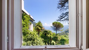 A window with a view of a lush garden, a building, and distant mountains.