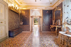 Una habitación ornamentada con suelo estampado, un banco, una mesa con una estatua y un espejo con marco decorativo.