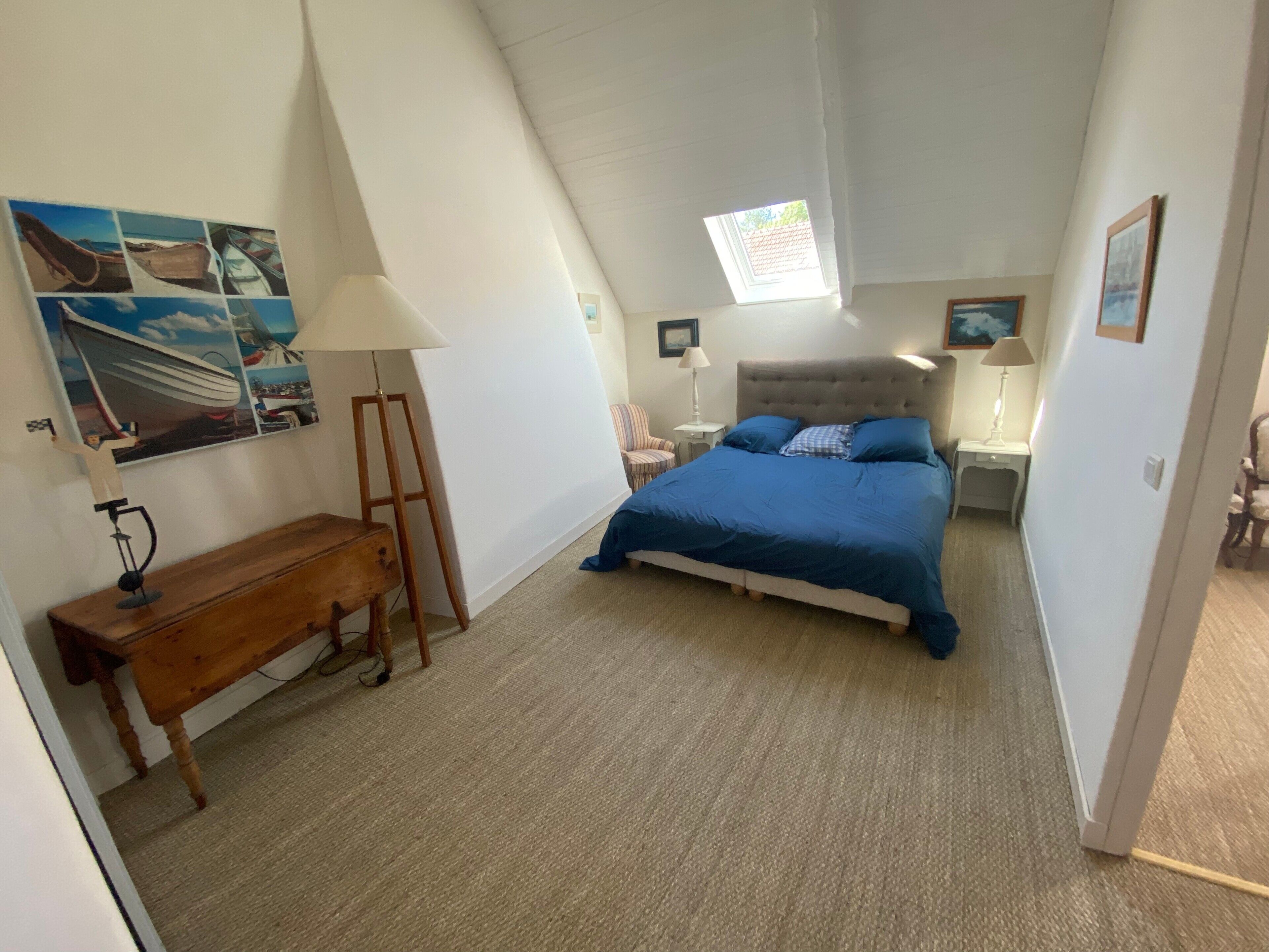 Une chambre à coucher avec un lit, un bureau, une chaise, une lampe et un tableau au mur.