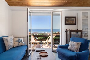 Ein Balkon mit Blick auf das Meer, ein blaues Sofa, ein blauer Sessel und ein Tisch mit einem Glas und einem Teller.