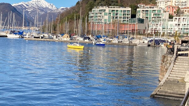 Un puerto deportivo con barcos, una montaña al fondo y edificios a lo largo de la costa.