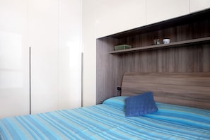 Een slaapkamer met een bed, een houten hoofdbord, een plank met spullen en een kledingkast.