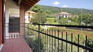 Un balcón con barandilla metálica, suelo de ladrillo y vistas a una zona residencial con casas y vegetación.