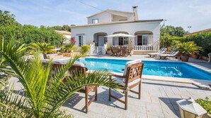 Een villa met zwembad, tuinmeubilair en weelderige begroeiing.