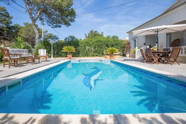 Una piscina con un mosaico de delfín, rodeada de mobiliario exterior y plantas en macetas.