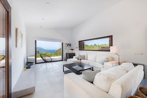 A modern living room with a large window, a sofa, a coffee table, and a view of the sea.