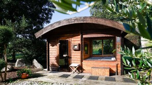 A wooden cabin with a curved roof, a wooden deck, and a small seating area. - Unique Family Loft in Former Stable with Sauna and Jacuzzi (Cléguérec)