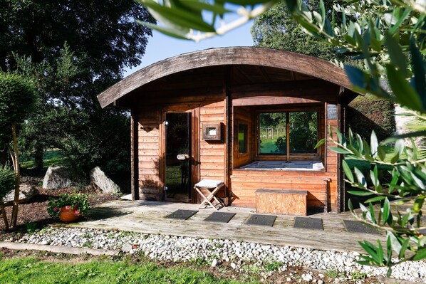 A wooden cabin with a curved roof, a wooden deck, and a small seating area.