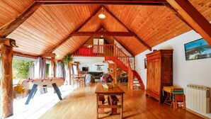 A spacious loft with a high ceiling, wooden beams, a dining area, a staircase, and a view of the outdoors. - Unique Family Loft in Former Stable with Sauna and Jacuzzi (Cléguérec)