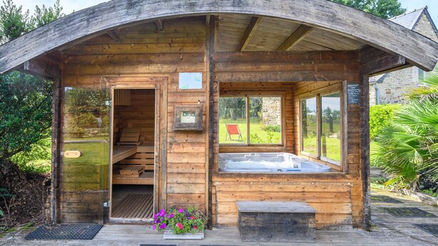 A wooden cabin with a hot tub, a bench, and a view of the garden. - Unique Family Loft in Former Stable with Sauna and Jacuzzi (Cléguérec)