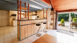A kitchen with wooden bar stools, a microwave, and a stone accent wall. - Unique Family Loft in Former Stable with Sauna and Jacuzzi (Cléguérec)