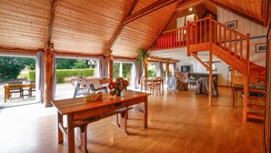 A spacious interior with a wooden ceiling, a dining area with a table and chairs, a staircase, and a view of the outdoors. - Unique Family Loft in Former Stable with Sauna and Jacuzzi (Cléguérec)