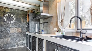 A kitchen with a stone backsplash, stainless steel cabinets, a built-in oven, and a window with sheer curtains.