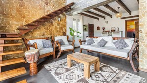 A stone wall, wooden staircase, wooden chairs, a sofa, a wooden table, and a patterned rug in a room.
