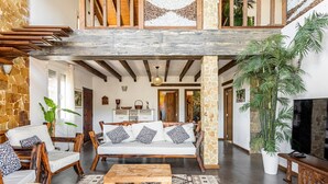 A spacious living area with a wooden bench, a sofa with patterned cushions, and a large potted plant.