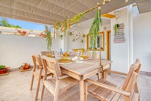 A wooden dining table set with chairs, surrounded by potted plants and hanging greenery.