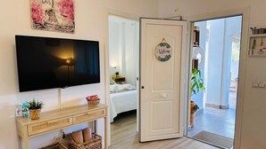 Ett hotellrum med en TV, en säng, ett avlastningsbord med korgar, en välkomstskylt och utsikt över omgivningarna.