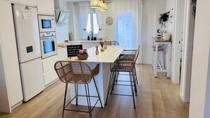 Ett modernt kök med en central köksö, barstolar, en hängande lampa och en klocka på väggen.