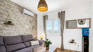 Un salon comprenant un canapé, une table basse, un luminaire suspendu, un distributeur d’eau et un climatiseur fixé au mur.