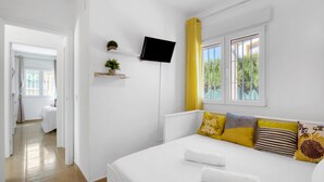Une chambre à coucher avec un lit, une télévision, une fenêtre avec des rideaux, une table de chevet avec une plante, et une vue sur l’extérieur.