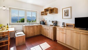 Une cuisine avec des meubles en bois, une table à manger avec des chaises, un téléviseur et une fenêtre donnant sur les montagnes.