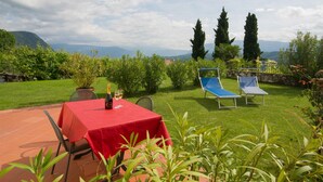 Une terrasse avec une table rouge, deux fauteuils bleus et une bouteille de vin.