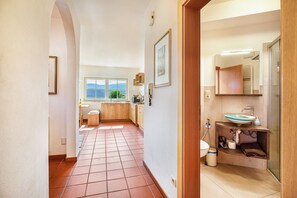 A hallway leading to a kitchen with a window, a bathroom with a sink and mirror, and a tiled floor. - Apartment 'Aurora' with Mountain View, Private Terrace and Wi-Fi (Kaltern)