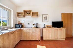 A kitchen with wooden cabinets, a microwave, a toaster, a coffee maker, and a television on a wooden stand. - Apartment 'Aurora' with Mountain View, Private Terrace and Wi-Fi (Kaltern)
