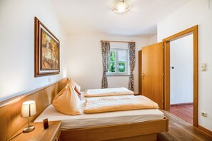 A bedroom with a wooden bed, a bedside table with a lamp, a window with curtains, and a door. - Apartment 'Aurora' with Mountain View, Private Terrace and Wi-Fi (Kaltern)