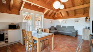 Un espacio habitable amplio con techo de madera, una mesa de comedor con sillas, un sofá gris y una zona de cocina con microondas.
