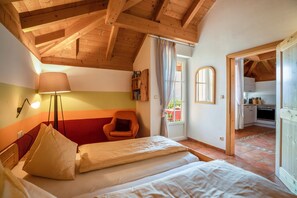 Ein Schlafzimmer mit Bett, Stuhl, Lampe und Blick auf eine Küche.