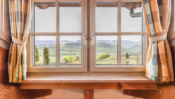 Una ventana con vistas a colinas ondulantes y un banco de madera debajo.