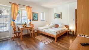 A bedroom with a wooden bed, a desk, a chair, a small table, and a window with curtains. - Studio 'Vitis' with Mountain View, Private Terrace and Wi-Fi (Kaltern)