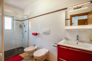 A bathroom with a glass shower enclosure, a bidet, a toilet, and a vanity with a mirror.