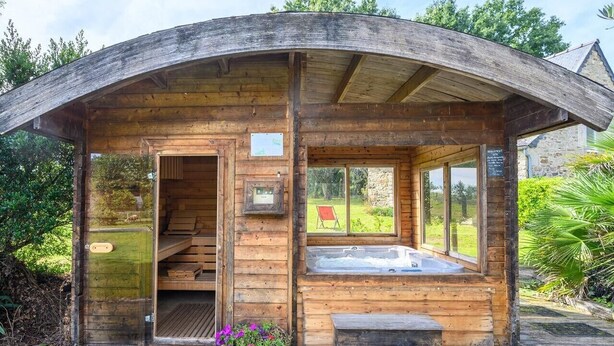Eine Holzhütte mit gewölbter Dachform, einem Whirlpool und einer kleinen Sitzgelegenheit im Freien.