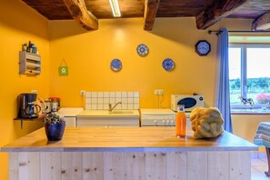 A kitchen with a wooden countertop, a coffee machine, a microwave, and a window with a view of greenery.