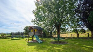 Ein Spielplatz mit Rutsche und Schaukeln, umgeben von Rasen und Bäumen.