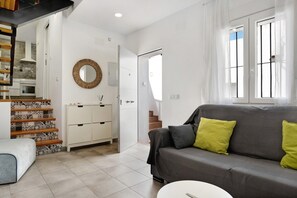 Un salon moderne avec un canapé gris, un meuble blanc, un escalier et un grand miroir rond accroché au mur.