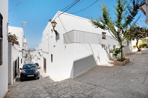A narrow street with a car parked on the left, white buildings, and a tree on the right. - Apartment "EleMe I" with Private Terrace & Wi-Fi (Vejer)