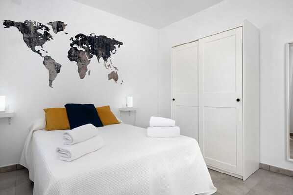Une chambre d’hôtel avec un lit, une carte du monde accrochée au mur, une armoire et une table de chevet avec une lampe.