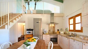 A kitchen with a refrigerator, stove, microwave, and coffee maker. There is a dining table with chairs and a window with curtains. - Country House 'Sa Volta' with Mountain View, Wi-Fi and Air Conditioning (selva)