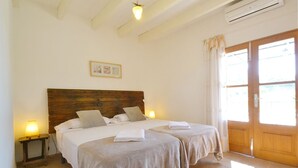 A bedroom with two beds, a wooden headboard, a small bedside table with a lamp, and a large window with curtains. - Country House 'Sa Volta' with Mountain View, Wi-Fi and Air Conditioning (selva)