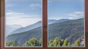 Ein Fenster mit Blick auf einen bewaldeten Bergrücken.