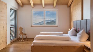Ein Zimmer mit Holzboden, einem Bett, einem Fenster mit Bergblick und einem Sessel.